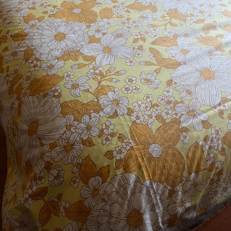 Pode incluir: Um len&ccedil;ol de cama com padr&atilde;o floral amarelo e branco em estilo vintage.
