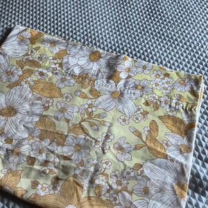 Pode incluir: Um tecido de estampa floral amarelo e branco com um padr&atilde;o de flores grandes. O tecido tem um toque vintage e seria perfeito para uma variedade de projetos de costura.