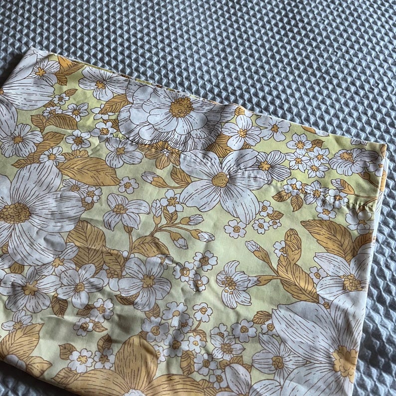Pode incluir: Um tecido de estampa floral amarelo e branco com um padr&atilde;o de flores grandes. O tecido tem um toque vintage e seria perfeito para uma variedade de projetos de costura.