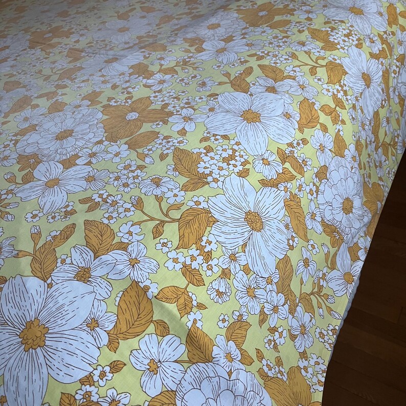 Pode incluir: Um len&ccedil;ol de cama com padr&atilde;o floral amarelo e branco com um grande desenho de flor branca.
