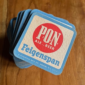 May include: A stack of blue and white cardboard coasters with the text "PON ALE. BEER Feigenspan C FEIGENSPAN BWG. CO. NEWARK, N.J." and a red circle with the text "PON" inside.