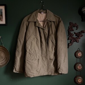 May include: A beige, lightweight jacket with a zipper closure and multiple pockets. The jacket has a relaxed fit and a classic design.