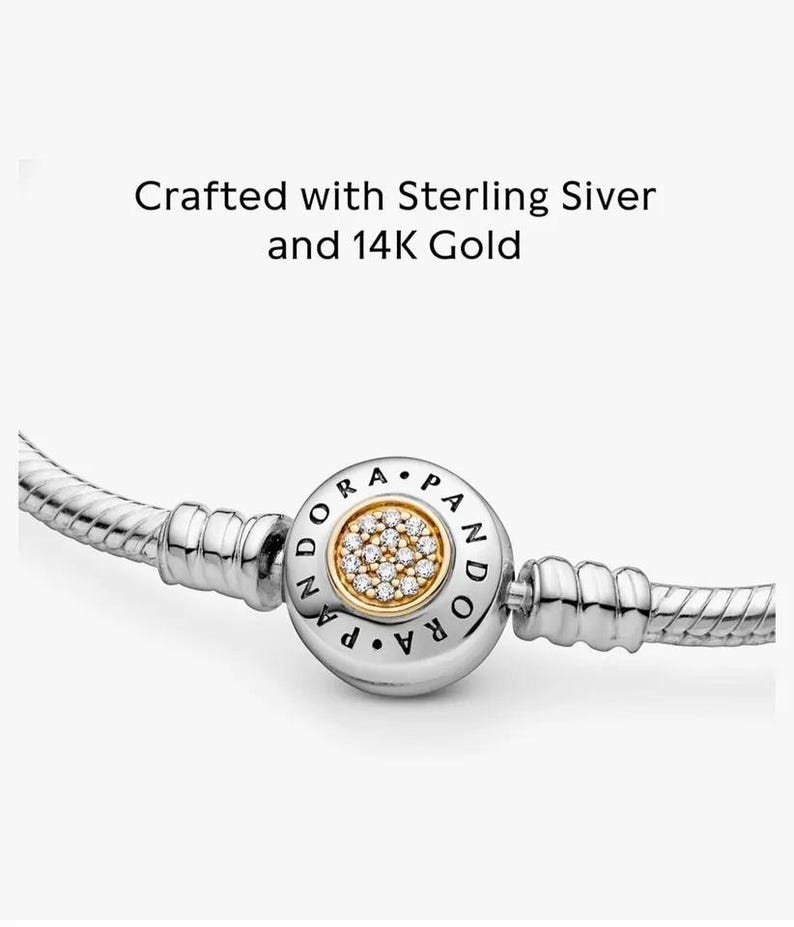May include: A silver and gold Pandora bracelet with a round charm that has a gold center with clear stones and the word "Pandora" written around the edge.