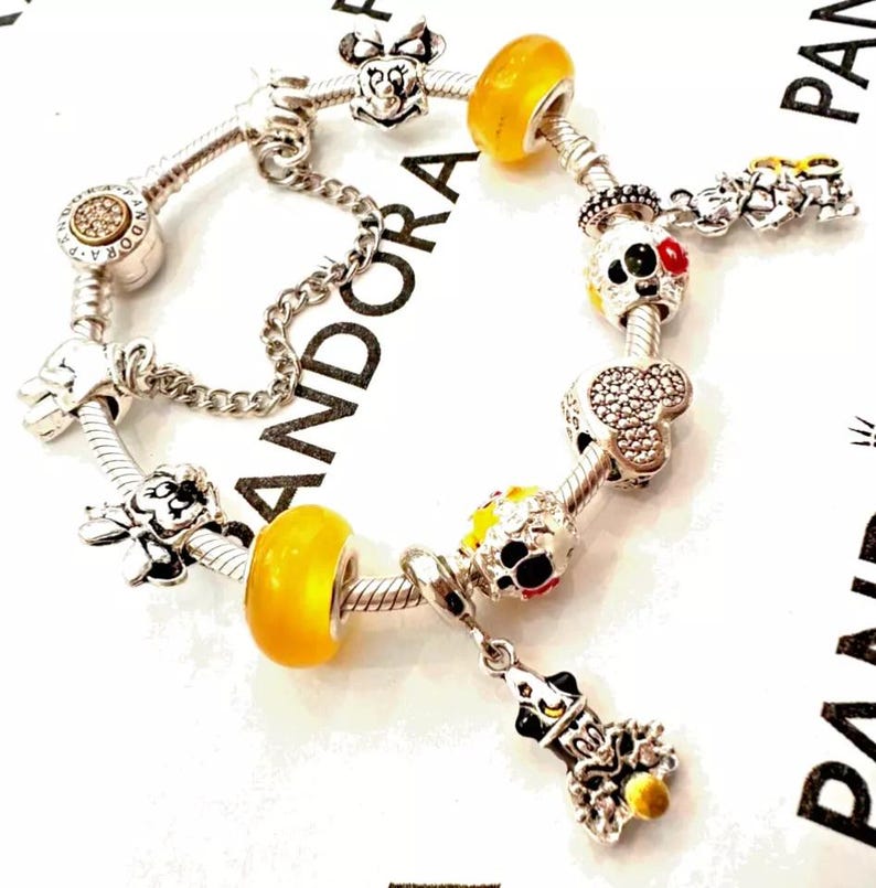 May include: A silver charm bracelet with a variety of Disney-themed charms, including Mickey Mouse, Minnie Mouse, and Goofy. The charms are silver, yellow, red, and black.