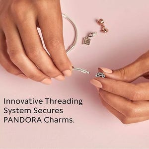 May include: A silver bracelet with a threading system that secures charms. The bracelet is shown being worn by a person, with a charm being added to the bracelet.