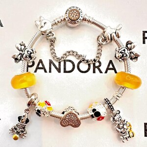 May include: A silver charm bracelet with a variety of Disney-themed charms, including Mickey Mouse, Minnie Mouse, and a heart charm. The bracelet is also adorned with yellow and red beads.