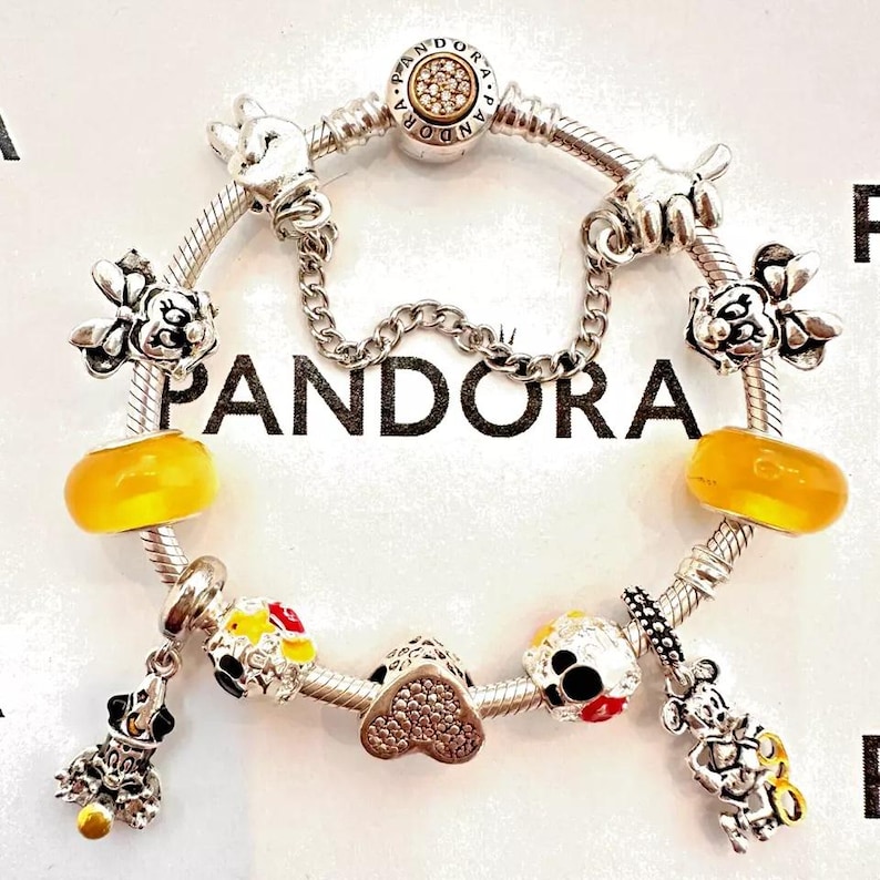 May include: A silver charm bracelet with a variety of Disney-themed charms, including Mickey Mouse, Minnie Mouse, and a heart charm. The bracelet is also adorned with yellow and red beads.