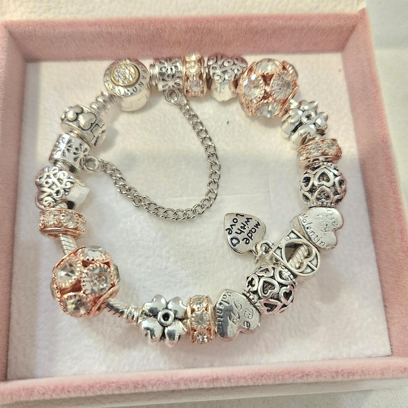 May include: A silver charm bracelet with a variety of charms, including hearts, flowers, and a charm that says "Made with Love".
