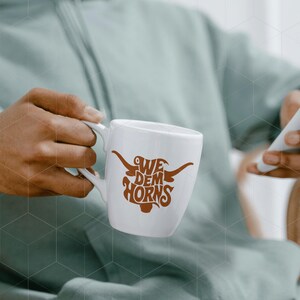 May include: White ceramic coffee mug with a brown graphic of a longhorn steer and the text "We Dem Horns".