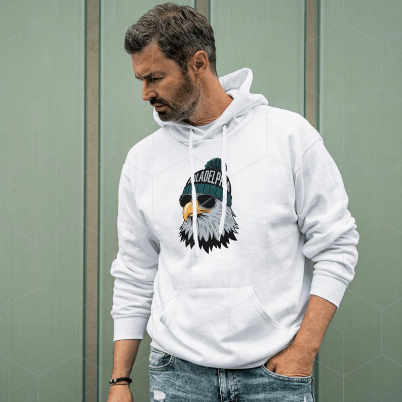 Peut inclure: Sweat-shirt &agrave; capuche blanc avec un graphique d'un aigle portant un chapeau vert et blanc et des lunettes de soleil. L'aigle porte un chapeau qui dit "Philadelphia".