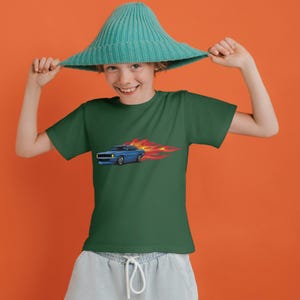 Pu&ograve; includere: Un giovane che indossa una maglietta verde con un'immagine di un'auto blu e fiamme. La persona indossa un cappello blu turchese e tiene il cappello con entrambe le mani.