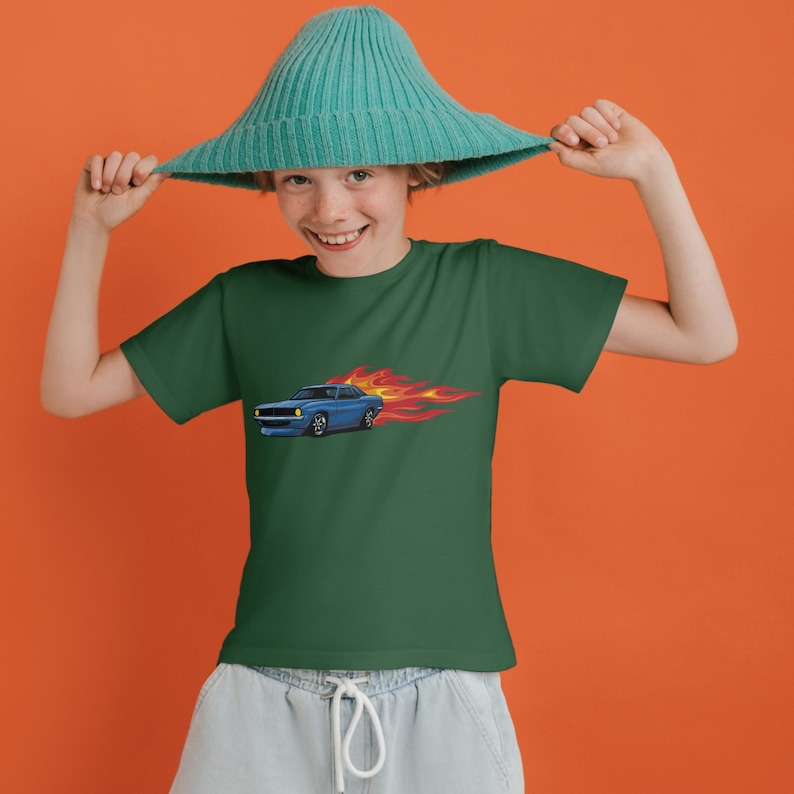 Pu&ograve; includere: Un giovane che indossa una maglietta verde con un'immagine di un'auto blu e fiamme. La persona indossa un cappello blu turchese e tiene il cappello con entrambe le mani.