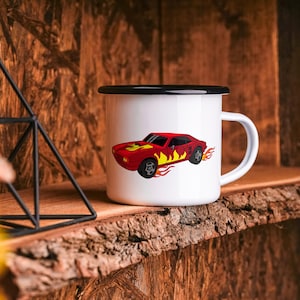 Pu&ograve; includere: Tazza in smalto bianco con bordo e manico neri. La tazza presenta un'auto rossa con fiamme gialle su sfondo bianco.
