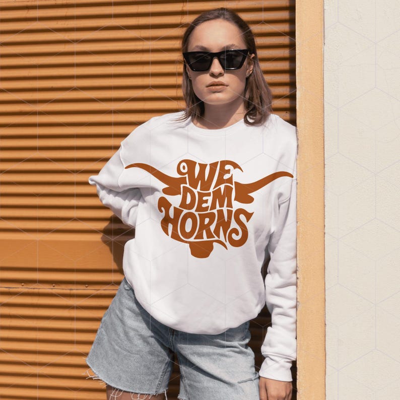 May include: White sweatshirt with a brown graphic of a longhorn steer with the text "We Dem Horns" on it.