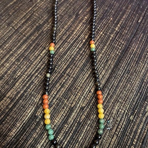 May include: A black beaded necklace with a black pendant. The beads are interspersed with orange, yellow, and green beads.