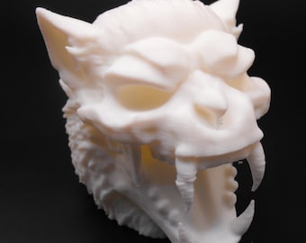 May include: A 3D-printed, off-white sculpture of a snarling beast's head. The sculpture features sharp fangs, detailed fur texture, and pointed ears. The mouth is wide open, showcasing the teeth. The background is black.