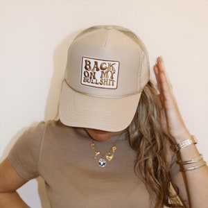 Puede incluir: Una gorra de camionero beige con un parche marrón que dice "Back on my Bullshit".