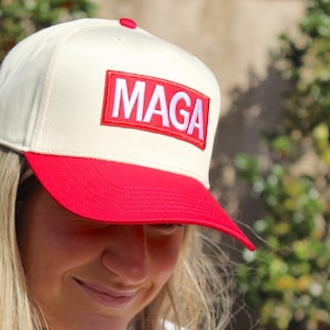May include: A white and red baseball cap with a white patch that says "MAGA" in red letters.