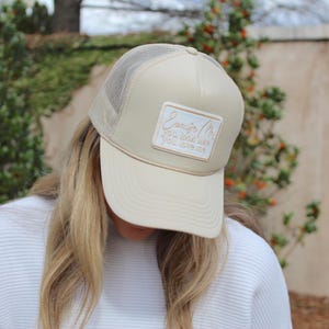 May include: A beige trucker hat with a mesh back and a white patch that says "Excuse me, you look like you love me".