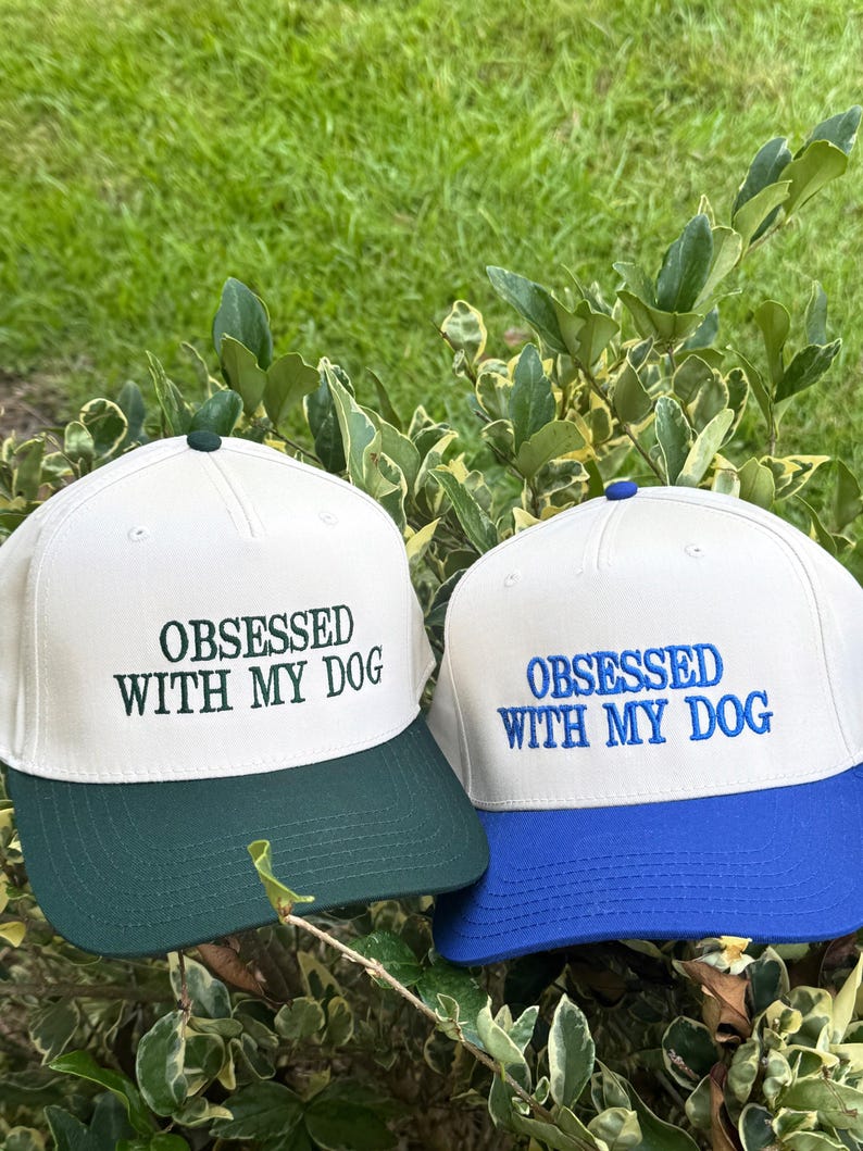 May include: Two baseball caps with the text "OBSESSED WITH MY DOG". One cap has a white crown and a green brim, the other has a white crown and a blue brim. Both caps are embroidered with the text in matching colors.