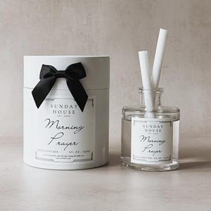 May include: A white cylindrical room diffuser with a black bow and a clear glass diffuser with white reeds. Both feature the text "Morning Prayer" and "Sunday House". The room diffuser is 5 fl oz / 147ml.