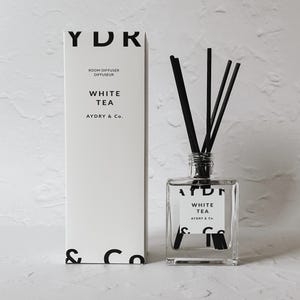 May include: White tea scented room diffuser with black reeds in a clear glass bottle and a white box with black text that reads "YDR Room Diffuser Diffuseur White Tea AYDRY & Co."