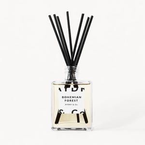 May include: A clear square glass reed diffuser bottle filled with light-colored liquid. The white label features the black text AYDRY & Co. and BOHEMIAN FOREST. Several thin black reeds are inserted into the bottle neck, extending upwards.