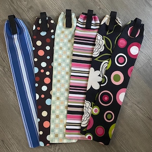 May include: Six fabric sleeves with different patterns, including stripes, polka dots, and geometric designs. Each sleeve has a black strap.