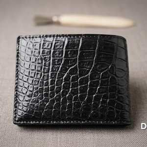May include: A black bifold wallet featuring a glossy, embossed crocodile skin texture. The wallet has visible stitching along the edges and the text DaliCraft. is printed in white in the lower right corner, with a blurred tool in the background.