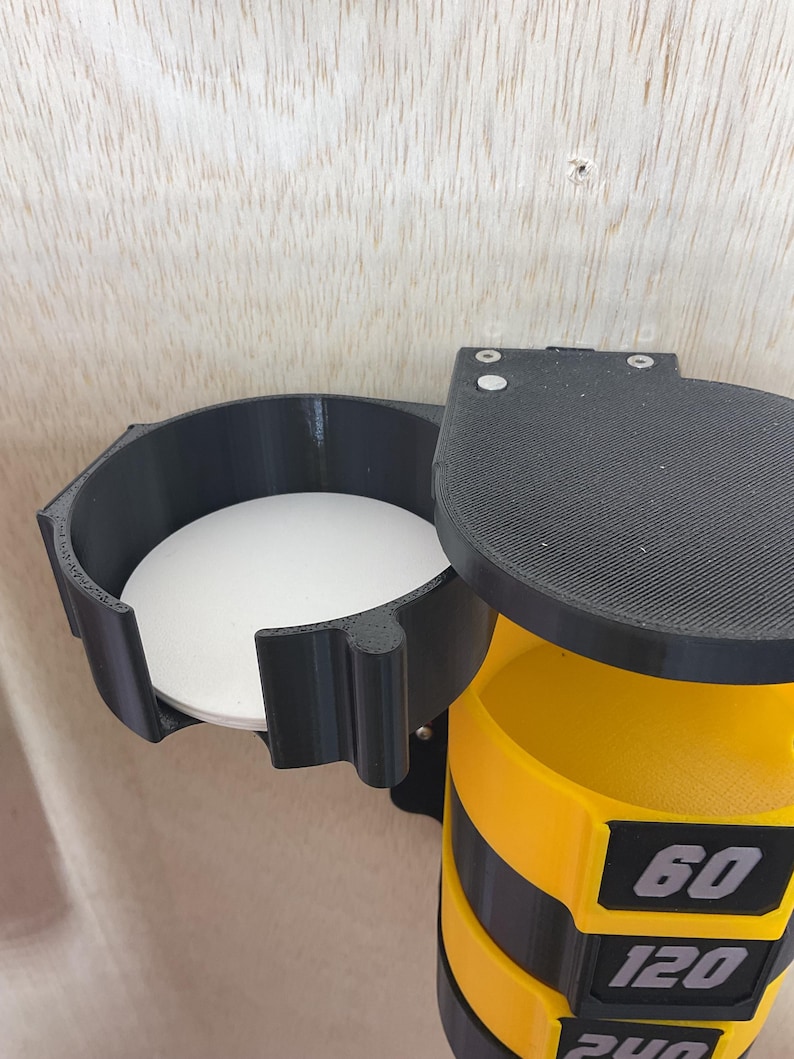 Puede incluir: Un soporte de pared negro y amarillo que presenta una secci&oacute;n circular con base blanca y una columna vertical con tres compartimentos amarillos apilados. Cada compartimento muestra una etiqueta negra con los n&uacute;meros 60, 120 y 240.