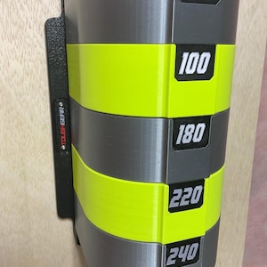 Puede incluir: Un organizador de almacenamiento montado en la pared con bandas horizontales alternas en gris y amarillo ne&oacute;n. La unidad incluye etiquetas rectangulares negras con los n&uacute;meros blancos 80, 100, 180, 220 y 240. Un panel lateral negro muestra TOUGHGEAR en rojo.