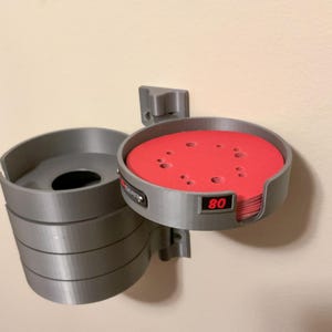 May include: A gray wall-mounted storage organizer for circular sanding discs. The unit features a stack of gray cylindrical holders with a prominent red sanding disc visible in the top compartment, which is clearly labeled with the number 80 in red.