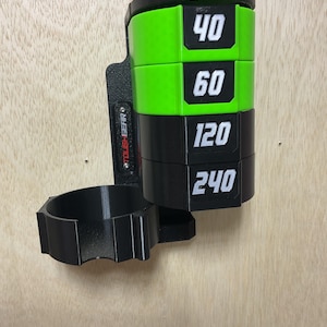 Puede incluir: Un organizador de pared negro y verde lima con una pila cil&iacute;ndrica de cuatro discos etiquetados con los n&uacute;meros 40, 60, 120 y 240 en blanco. La unidad incluye un soporte circular unido a una placa de montaje vertical con el texto TOUGHGEAR.