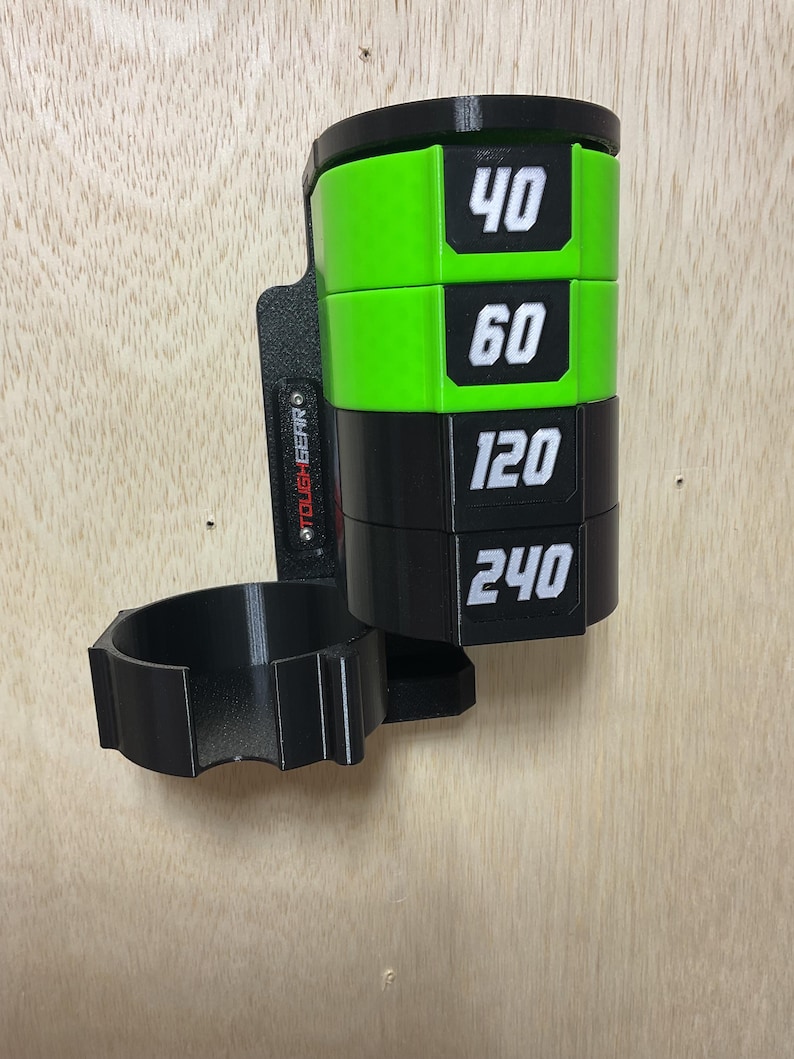 Puede incluir: Un organizador de pared negro y verde lima con una pila cil&iacute;ndrica de cuatro discos etiquetados con los n&uacute;meros 40, 60, 120 y 240 en blanco. La unidad incluye un soporte circular unido a una placa de montaje vertical con el texto TOUGHGEAR.