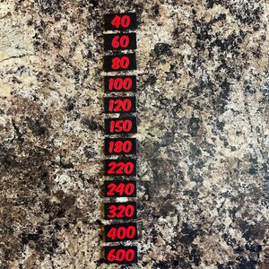 May include: A vertical column of twelve small, rectangular black labels, each featuring a bold red number. The numbers listed in descending order are 40, 60, 80, 100, 120, 150, 180, 220, 240, 320, 400, and 600, representing grit levels for sanding.