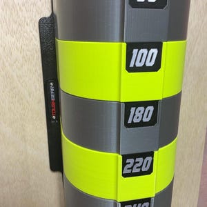 Puede incluir: Un estante de almacenamiento montado en la pared con secciones cil&iacute;ndricas alternas en gris y amarillo ne&oacute;n. Cada secci&oacute;n muestra una etiqueta rectangular negra con n&uacute;meros blancos: 80, 100, 180, 220 y 240. Una placa de montaje negra tiene la marca TOUGHGEAR.