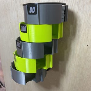 Puede incluir: Un estante de almacenamiento montado en la pared con cinco soportes semicirculares apilados en colores gris y amarillo ne&oacute;n alternos. Cada soporte tiene una etiqueta rectangular negra con los n&uacute;meros blancos 80, 100 y 180 impresos.