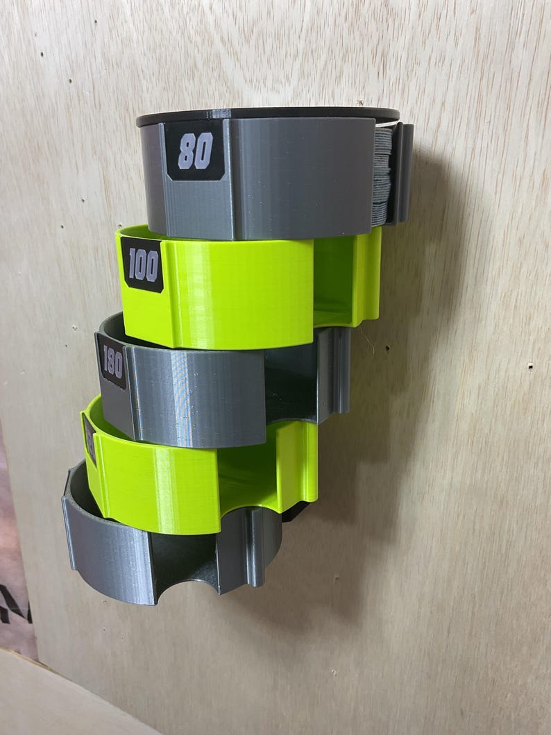 Puede incluir: Un estante de almacenamiento montado en la pared con cinco soportes semicirculares apilados en colores gris y amarillo ne&oacute;n alternos. Cada soporte tiene una etiqueta rectangular negra con los n&uacute;meros blancos 80, 100 y 180 impresos.