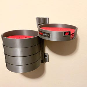 May include: A grey wall-mounted storage organizer with a pivoting arm featuring multiple circular compartments. The unit holds stacks of red circular sanding discs. One compartment displays the text TOUGHGEAR and the number 80 in red.