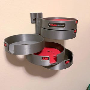May include: A gray wall-mounted organizer with multiple pivoting circular trays for sanding discs. Each tray features a red base and a black label with red text indicating grit sizes 80, 100, 180, 220, and 320. A black plate with the text TOUGHGEAR is attached.