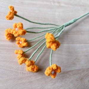 May include: A bouquet of crocheted orange flowers with green stems. The flowers have small white beads in the center.