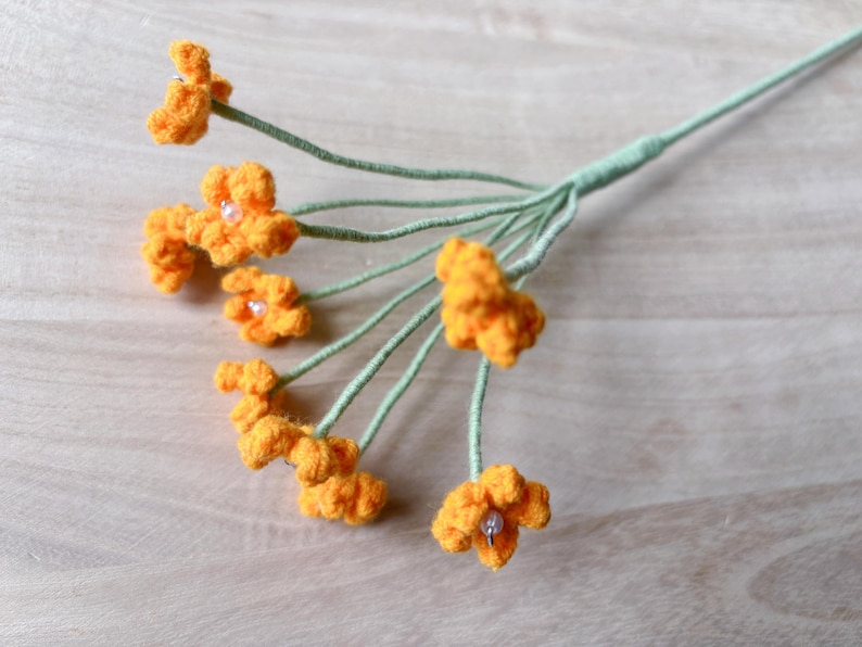 May include: A bouquet of crocheted orange flowers with green stems. The flowers have small white beads in the center.