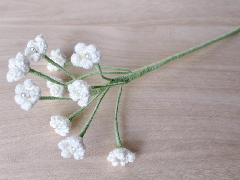 May include: A bouquet of white crocheted flowers with pearl centers on green stems.