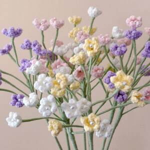 May include: A bouquet of crocheted flowers in shades of purple, pink, white, and yellow. The flowers are arranged in a vase and are a beautiful addition to any home.