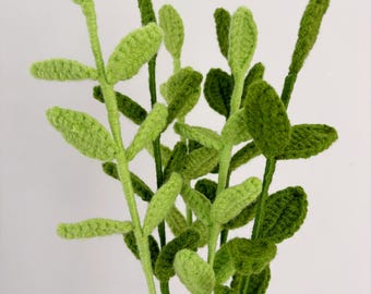 May include: A bunch of crocheted green leafy stems with a light green color. The stems are made of yarn and are arranged in a bouquet.