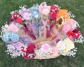 May include: A collection of colorful, crocheted flower bouquets in a woven basket. The bouquets feature various flower types in shades of pink, blue, red, and yellow, wrapped in decorative paper and tied with ribbons. White filler flowers add detail.