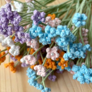 May include: A bunch of crocheted flowers in various colors, including orange, pink, purple, white, and blue. Each flower has a small white bead in the center.