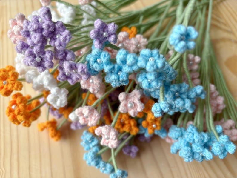 May include: A bunch of crocheted flowers in various colors, including orange, pink, purple, white, and blue. Each flower has a small white bead in the center.