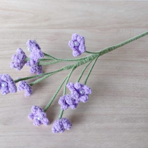 May include: A bunch of purple crocheted flowers with pearl centers on a green stem.