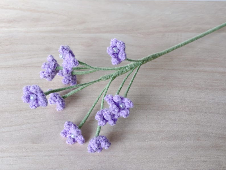 May include: A bunch of purple crocheted flowers with pearl centers on a green stem.